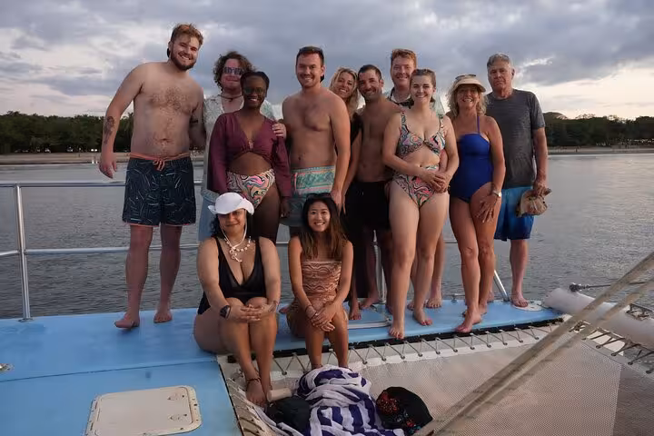Happy group of travelers posing on a Blue Dolphin catamaran during a sunset sailing tour.