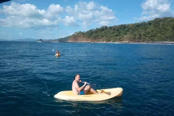 Tourists kayaking near a scenic coastline during the Blue Dolphin catamaran tour, with blue skies and clear waters.