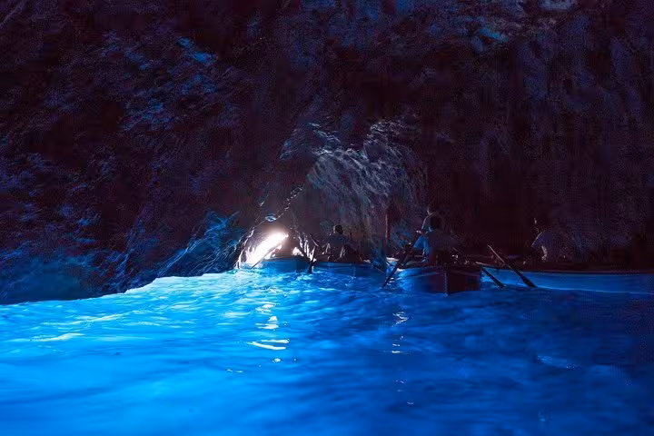 Visitors exploring the enchanting Blue Grotto's glowing waters on a small boat tour from Sorrento to Capri.