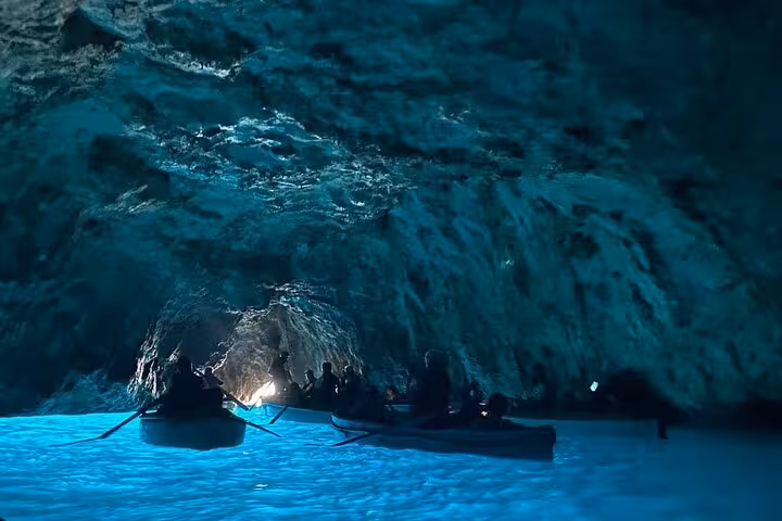 Tourists explore the enchanting Blue Grotto with its glowing blue waters on a small group boat tour from Sorrento.