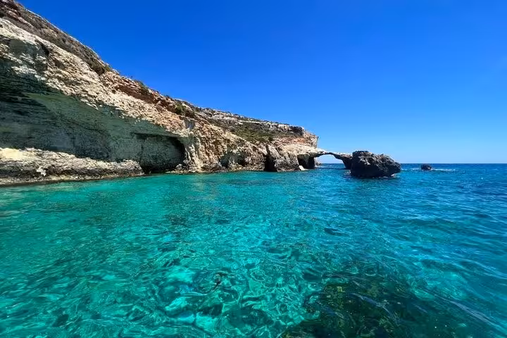 Crystal-clear Blue Lagoon waters by limestone cliffs and arch on Gozo Comino caves half-day Malta tour