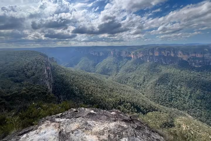 Stunning panoramic view of Blue Mountains' lush valleys and cliffs under a dramatic cloudy sky, perfect for private tours.