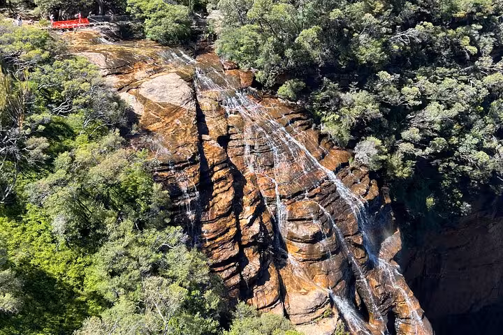 Aerial view of natural waterfall cascading over rocky cliffs in Blue Mountains surrounded by lush greenery.