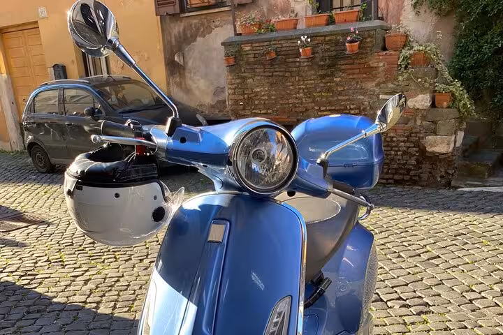 Close-up of a blue Vespa with helmet parked on cobblestone street in Rome, capturing the vintage charm of Italian travel.