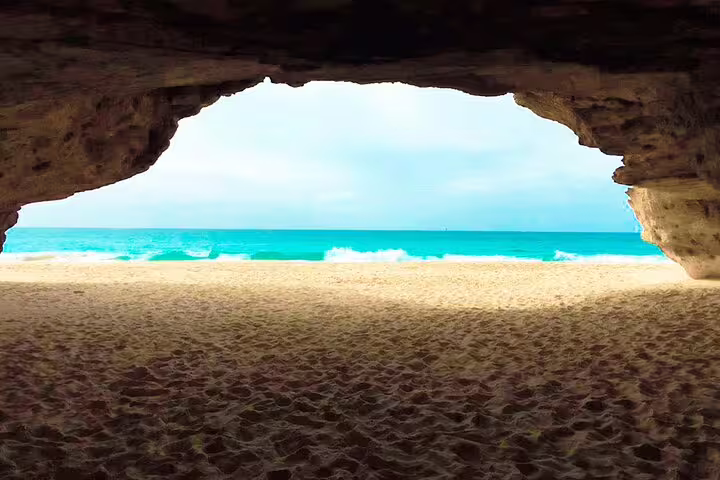 View from a cave opening to a tranquil beach with gentle waves and blue skies in Boa Vista adventure tour.