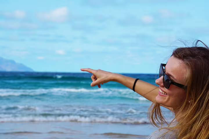 Smiling tourist wearing sunglasses pointing at the ocean on Boa Vista Island beach tour.