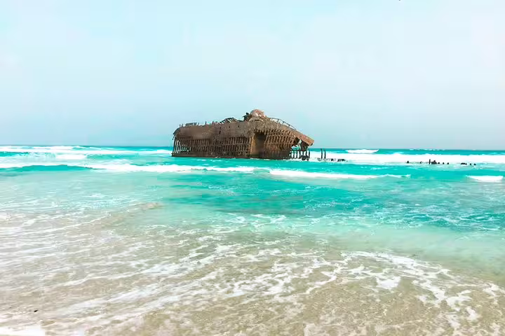 The rusted remains of a shipwreck on Boa Vista Island's coastline, surrounded by turquoise ocean waters.