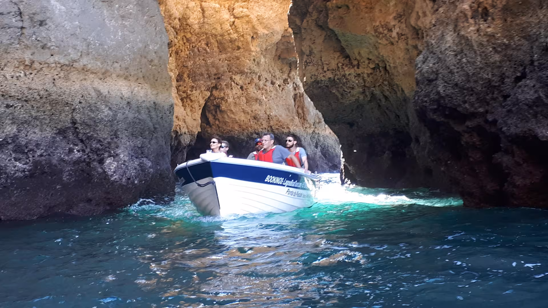 Small tour boat entering narrow Ponta da Piedade cave in Lagos, Portugal, surrounded by dramatic golden cliffs and turquoise sea