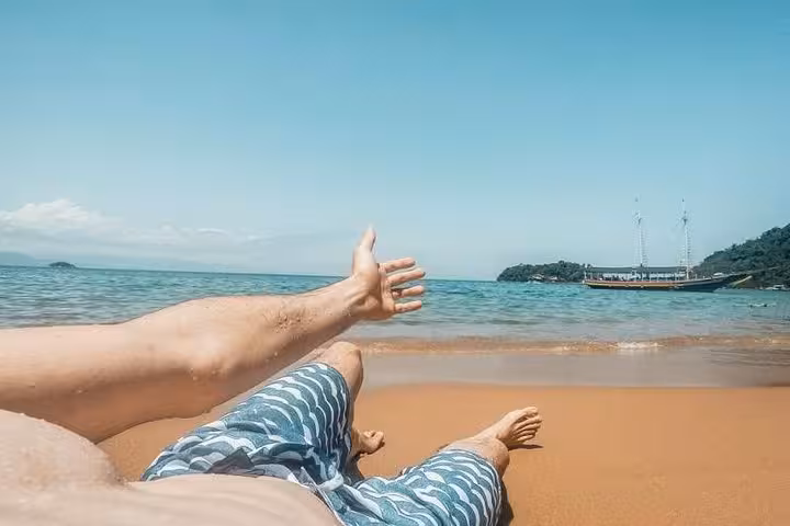 Relax on a sandy beach with a picturesque view of a traditional boat anchored in clear ocean waters.