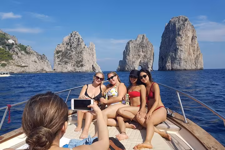 Group of friends enjoying a boat tour to Capri Island with Faraglioni rocks in the background, capturing unforgettable moments.