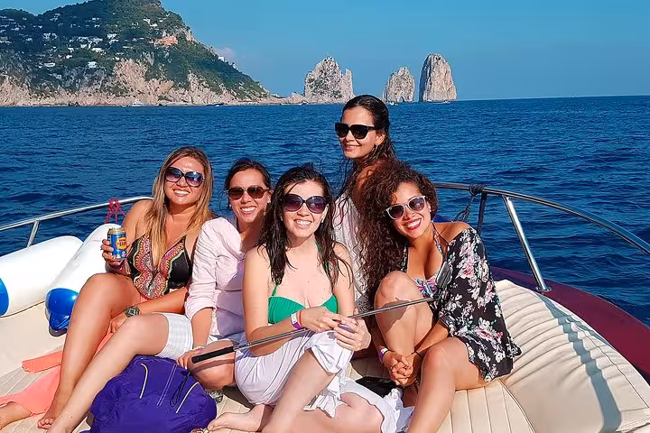 Group of friends enjoying a boat tour to Capri Island with Faraglioni rocks in the background.