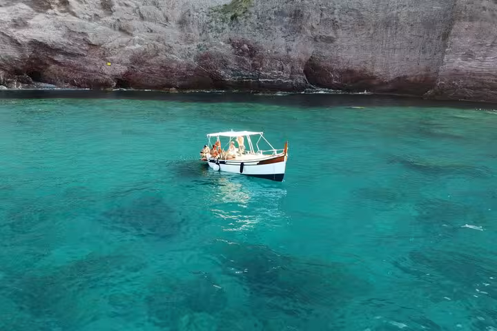 Tourists on a boat in crystal-clear waters near Lerici's rocky shoreline.