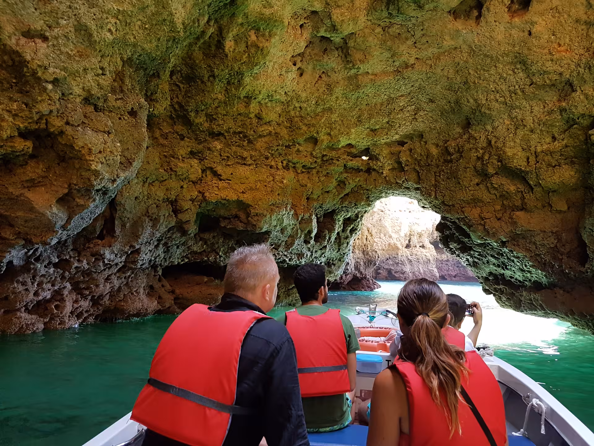 Small group in red life jackets on a boat tour gliding through emerald waters into Ponta da Piedade sea cave in Lagos