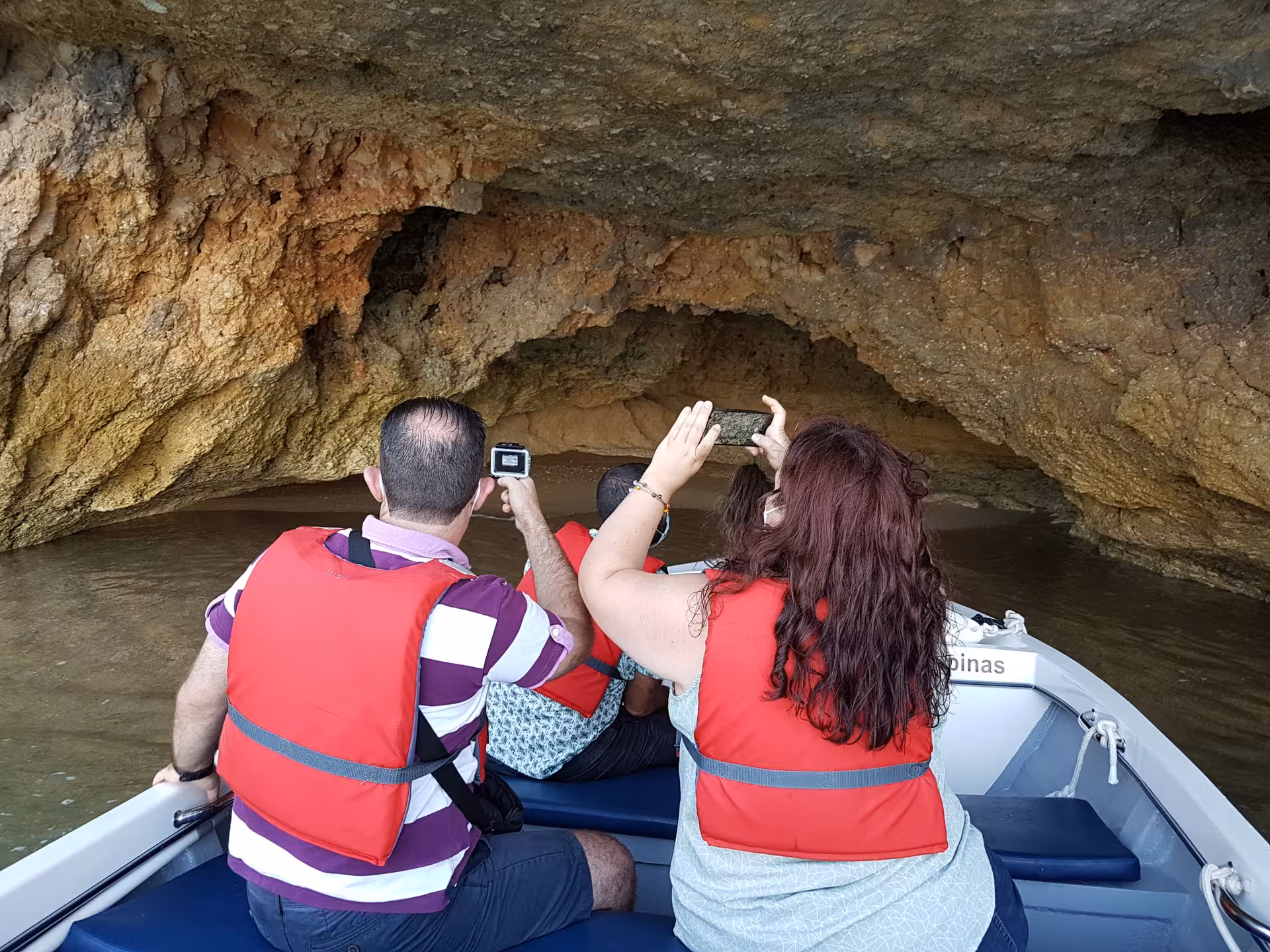 Small boat tour through Ponta da Piedade caves in Lagos, Portugal, with passengers in life jackets filming the rock formations