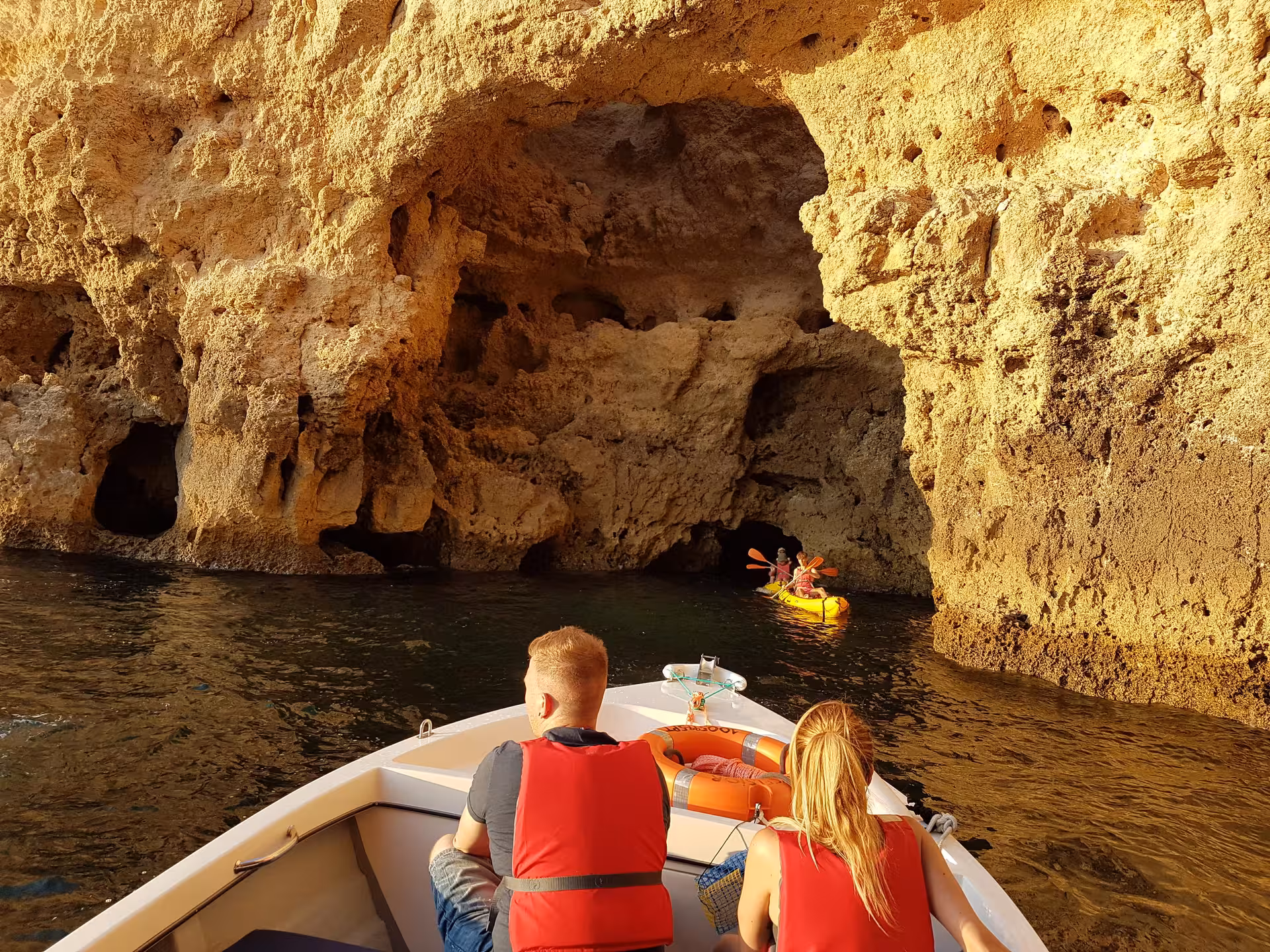 Boat tour passengers in Lagos approach golden Ponta da Piedade cliffs while kayakers paddle into a narrow sea cave entrance