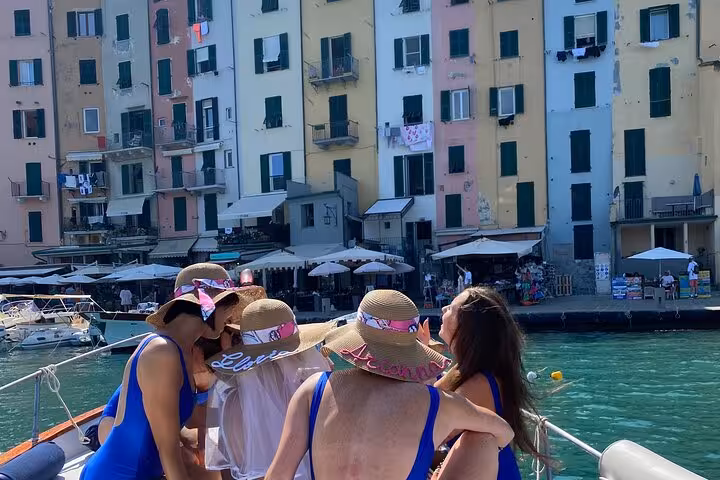 Group of friends enjoying a boat tour near colorful Portovenere buildings in La Spezia, Italy.