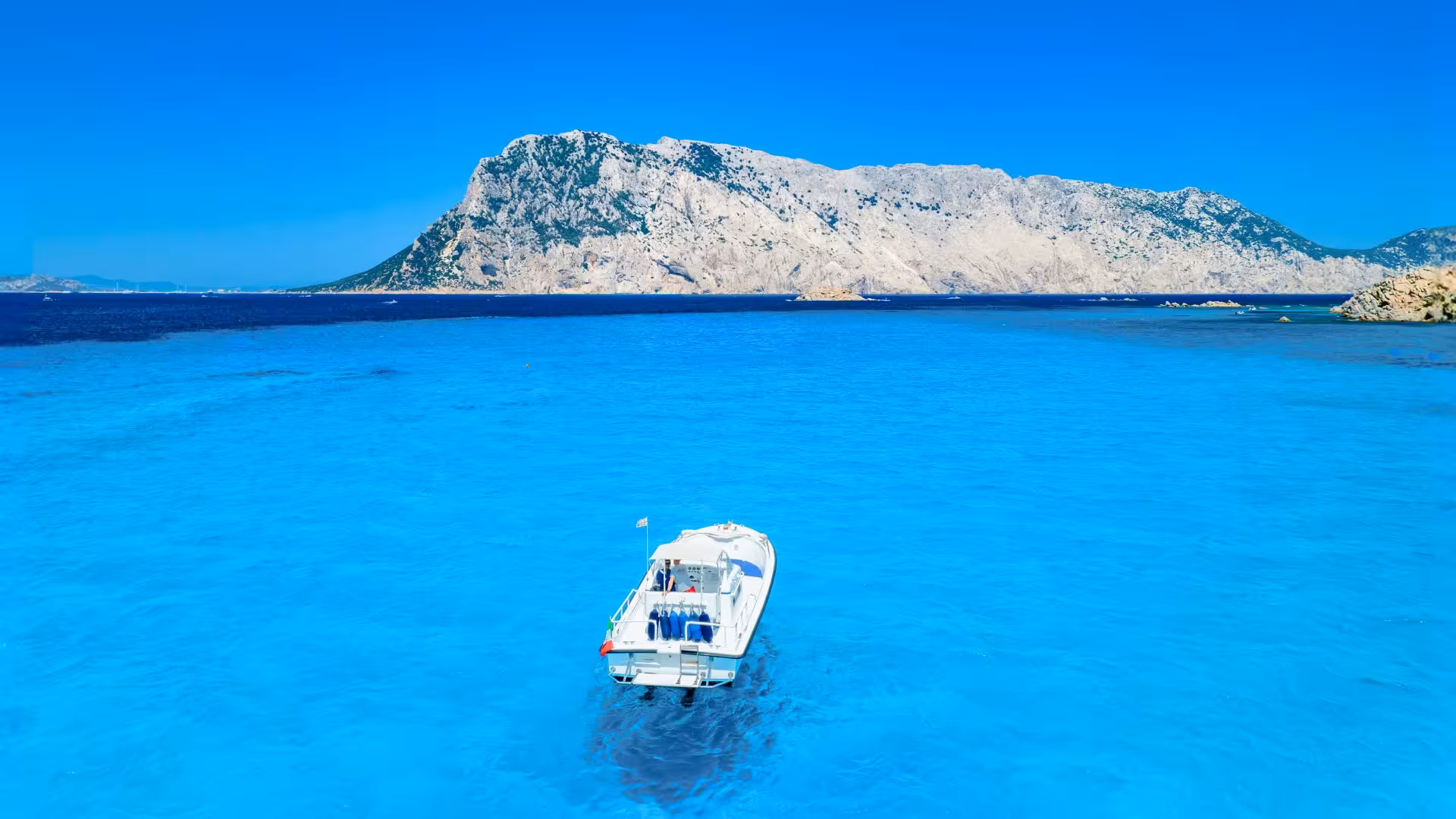 Boat on crystal-clear waters with Tavolara Island in the background during Porto San Paolo tour.