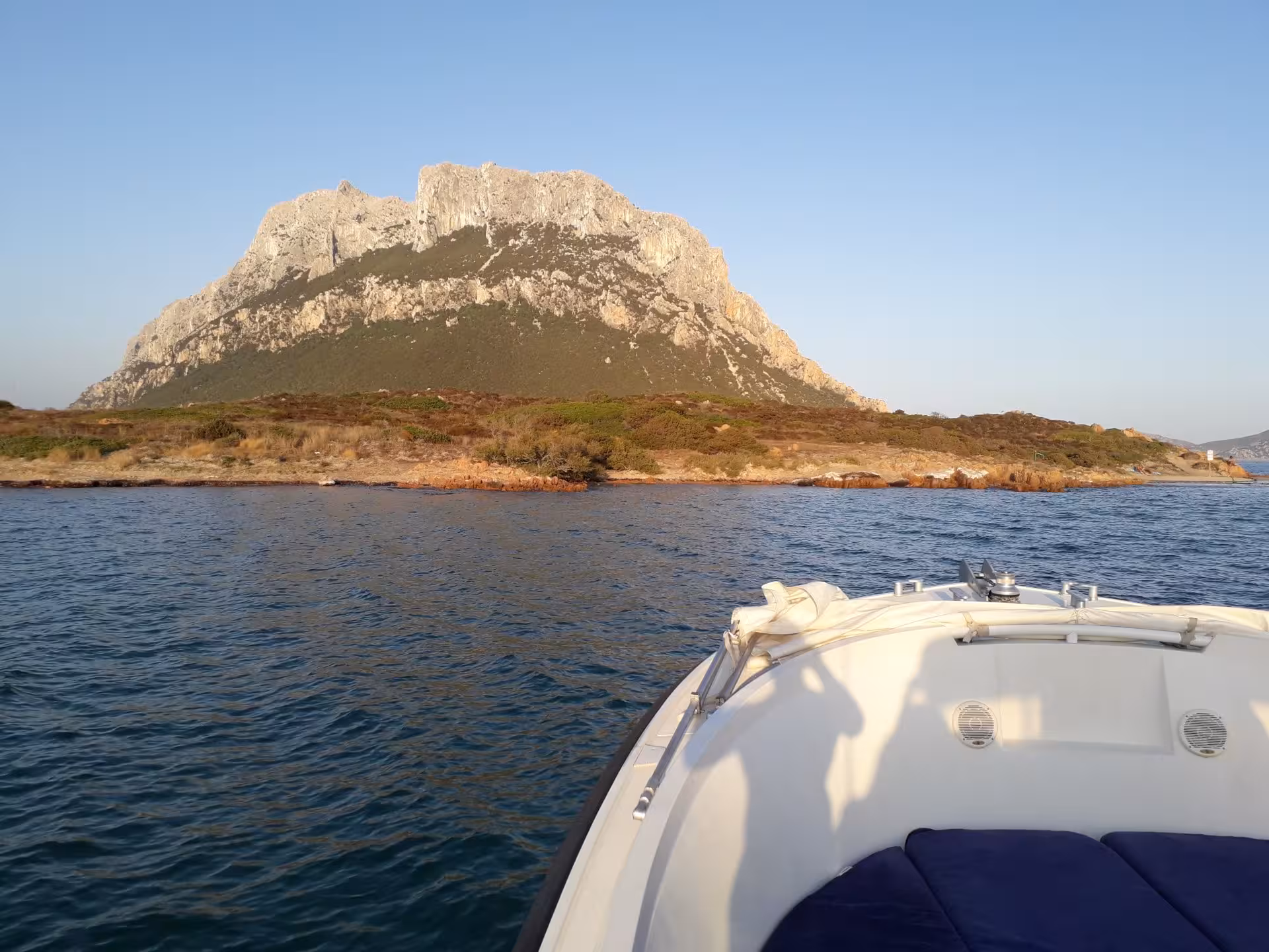 Boat approaching Tavolara Island's rocky shoreline at sunset on a Porto San Paolo tour.