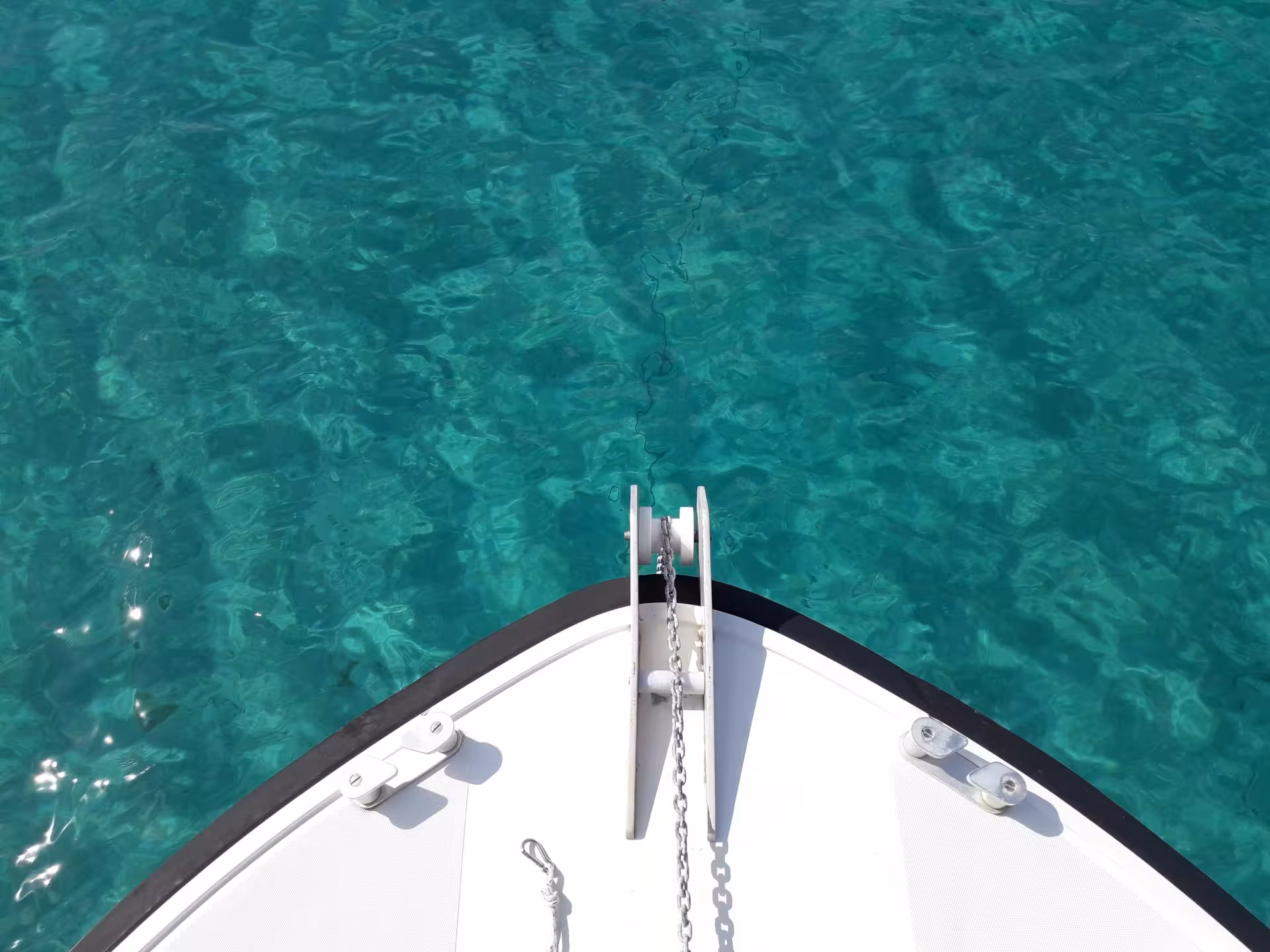 Bow of a boat cutting through crystal-clear turquoise waters near Tavolara Island on a Porto San Paolo tour.