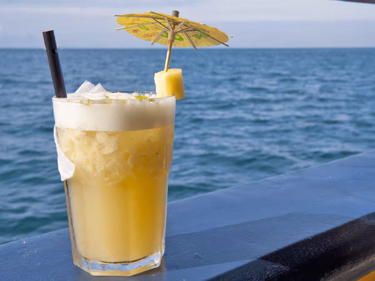 Refreshing caipirinha with a pineapple slice and umbrella on a boat, set against the ocean backdrop.
