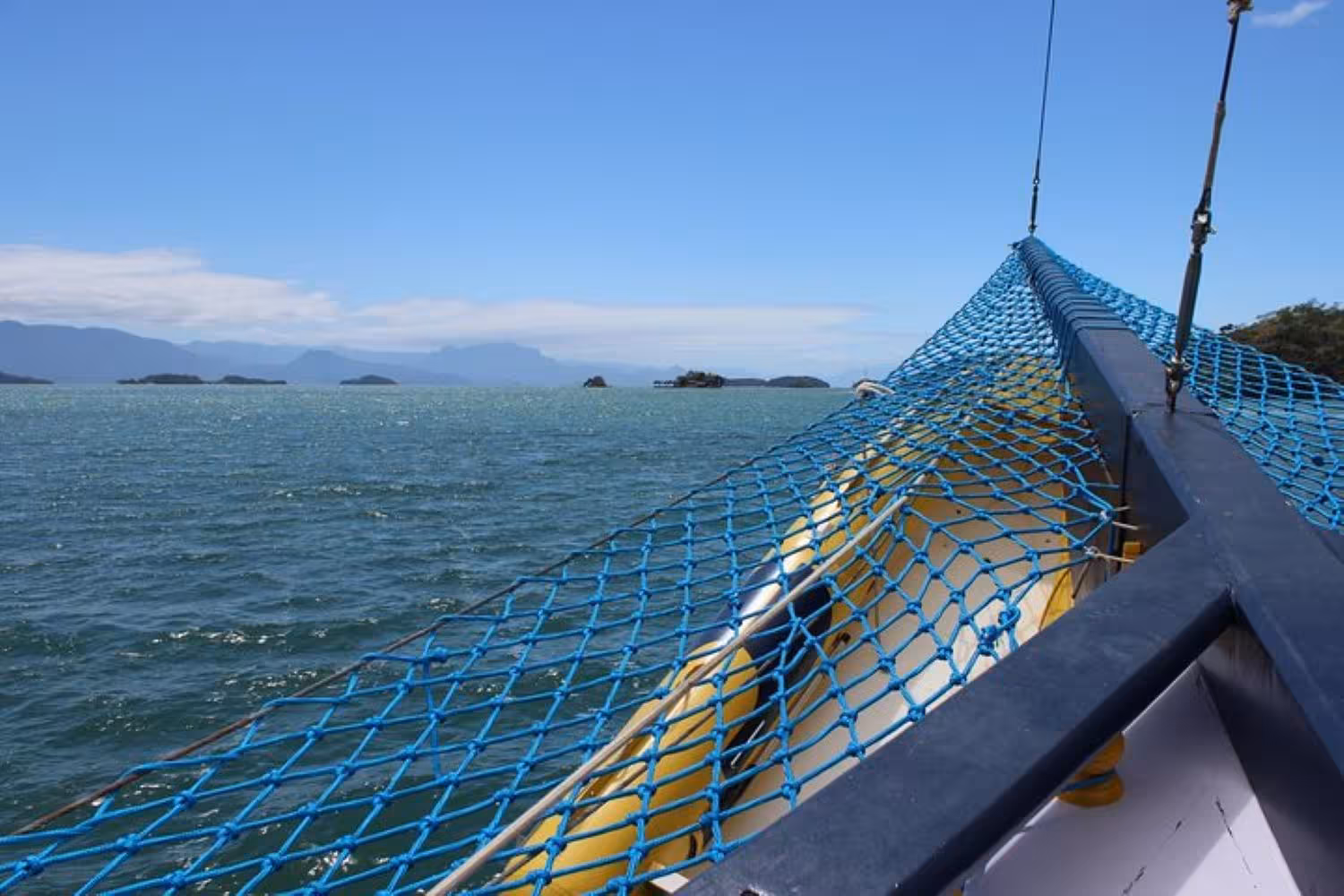 Scenic boat deck with blue netting overlooking calm ocean waters on a sunny day, perfect for a five-hour cruise.