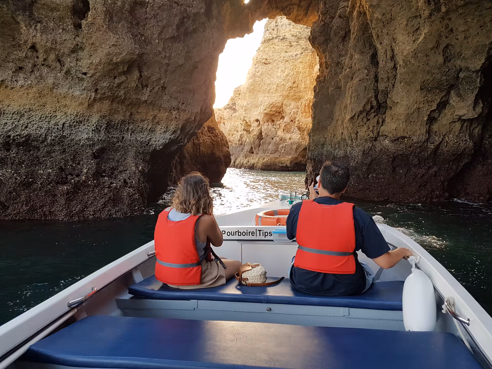 Tourists on a Lagos cave boat trip sailing toward a sunlit rock archway at Ponta da Piedade on the Algarve coast