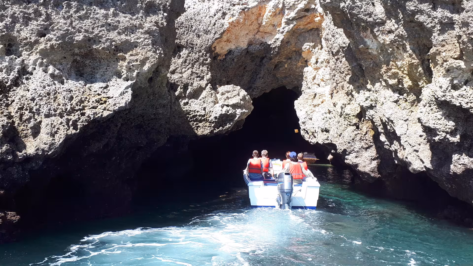 Tourists on a guided boat trip enter a dramatic sea cave at Ponta da Piedade, Lagos, surrounded by towering Algarve cliffs