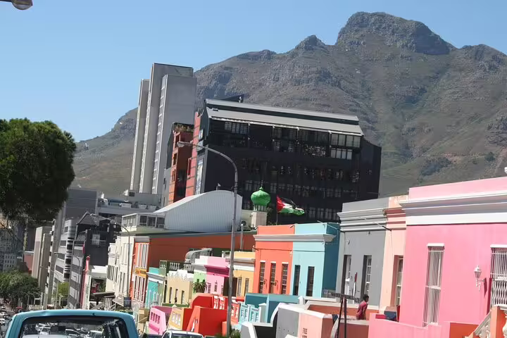 Colorful Bo-Kaap houses line a vibrant street in Cape Town, with Table Mountain towering in the background.