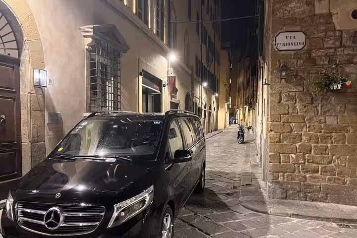 Luxurious black Mercedes van parked on a charming cobblestone street in Florence for private airport transfer.