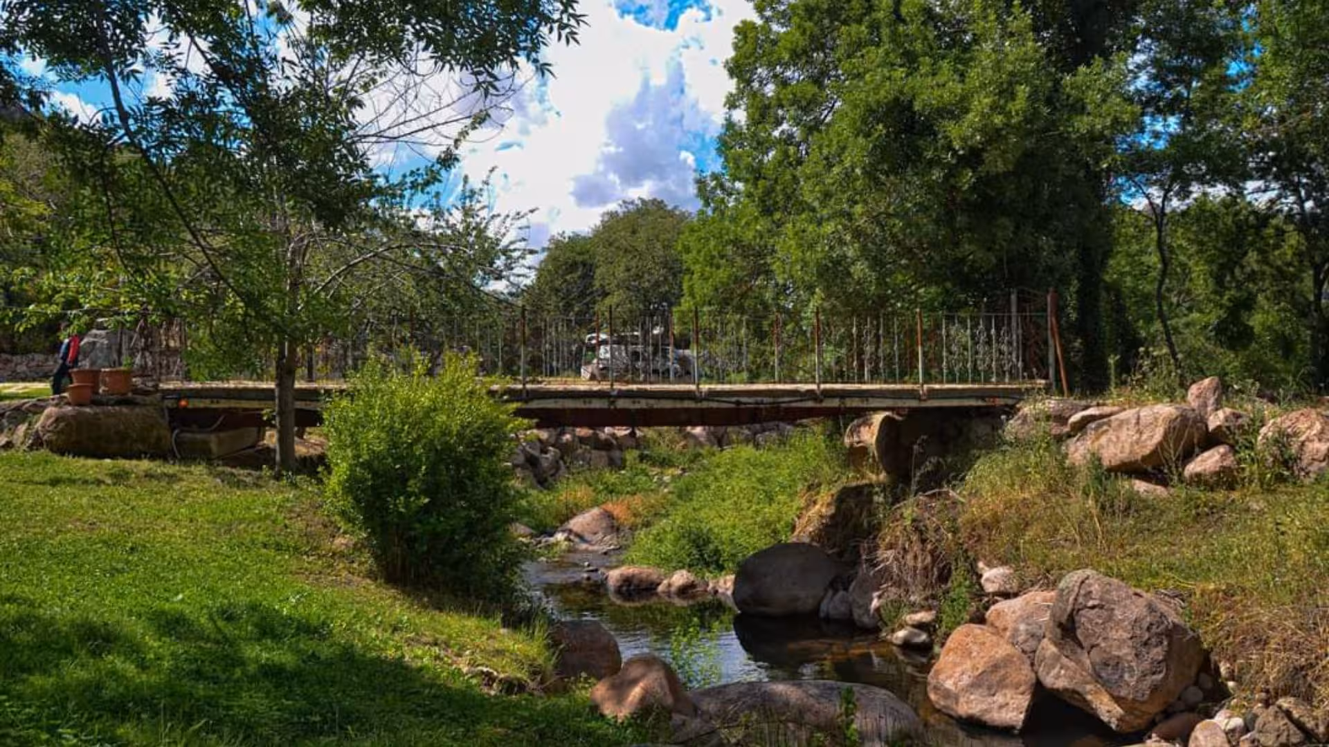 Scenic view of a rustic bridge over a stream surrounded by lush greenery at a Bonorva farm.