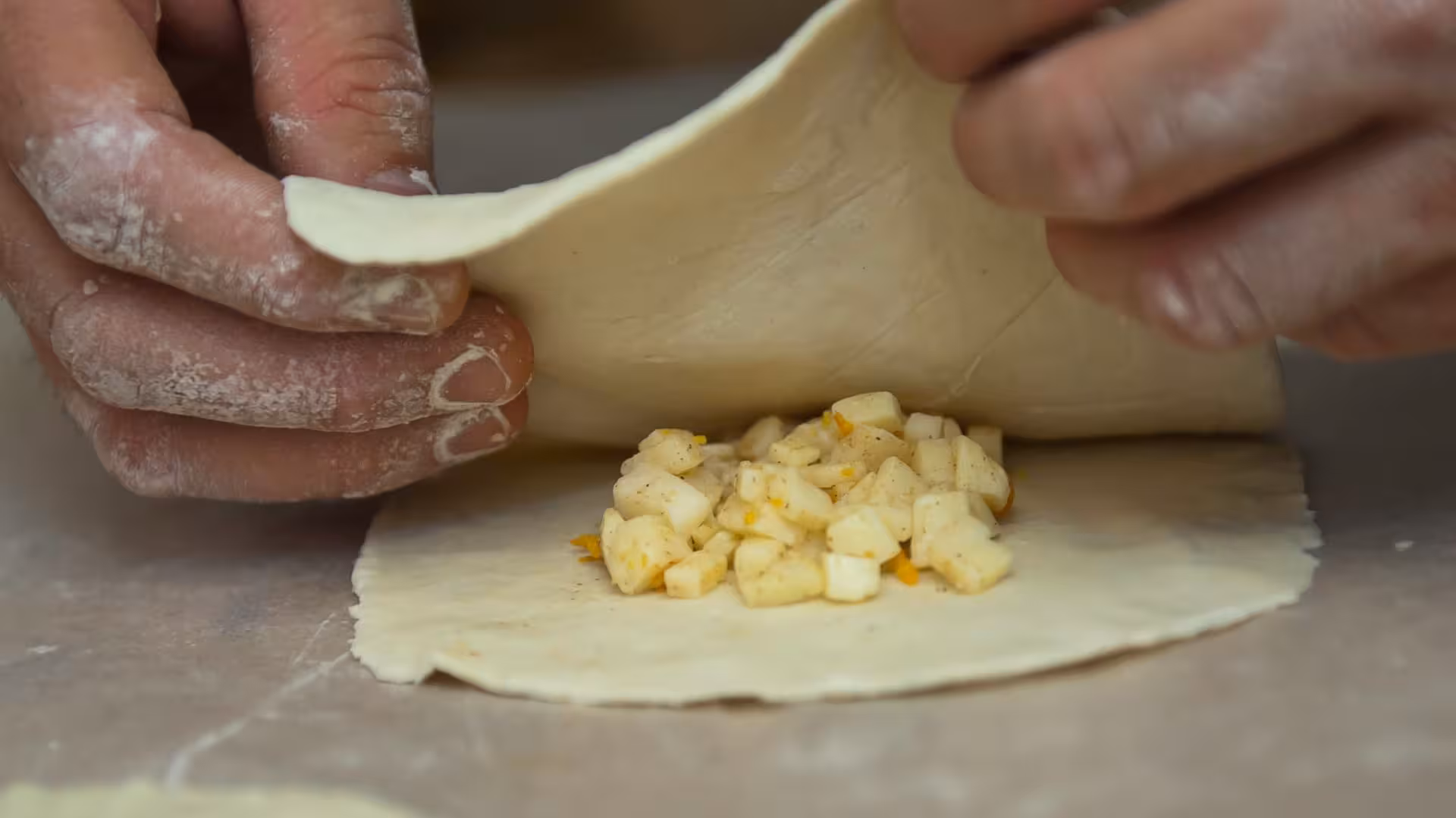 Close-up of hands folding dough with cheese and fruit filling during a seadas workshop in Bonorva, Sardinia.