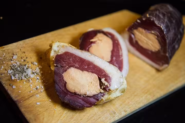 Slices of cured meat with foie gras on a wooden board, showcasing Bordeaux's culinary specialties.