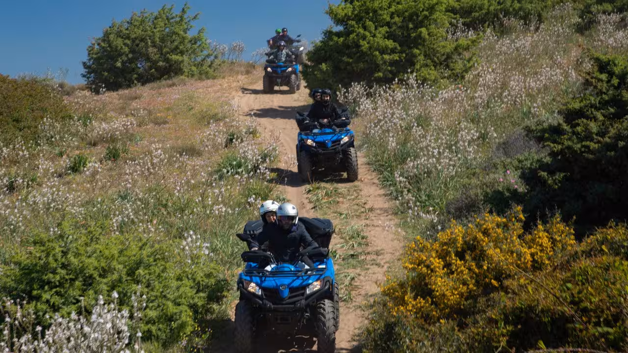 Adventurers on a scenic Bosa ATV tour ride through lush, flower-filled trails under a clear blue sky.