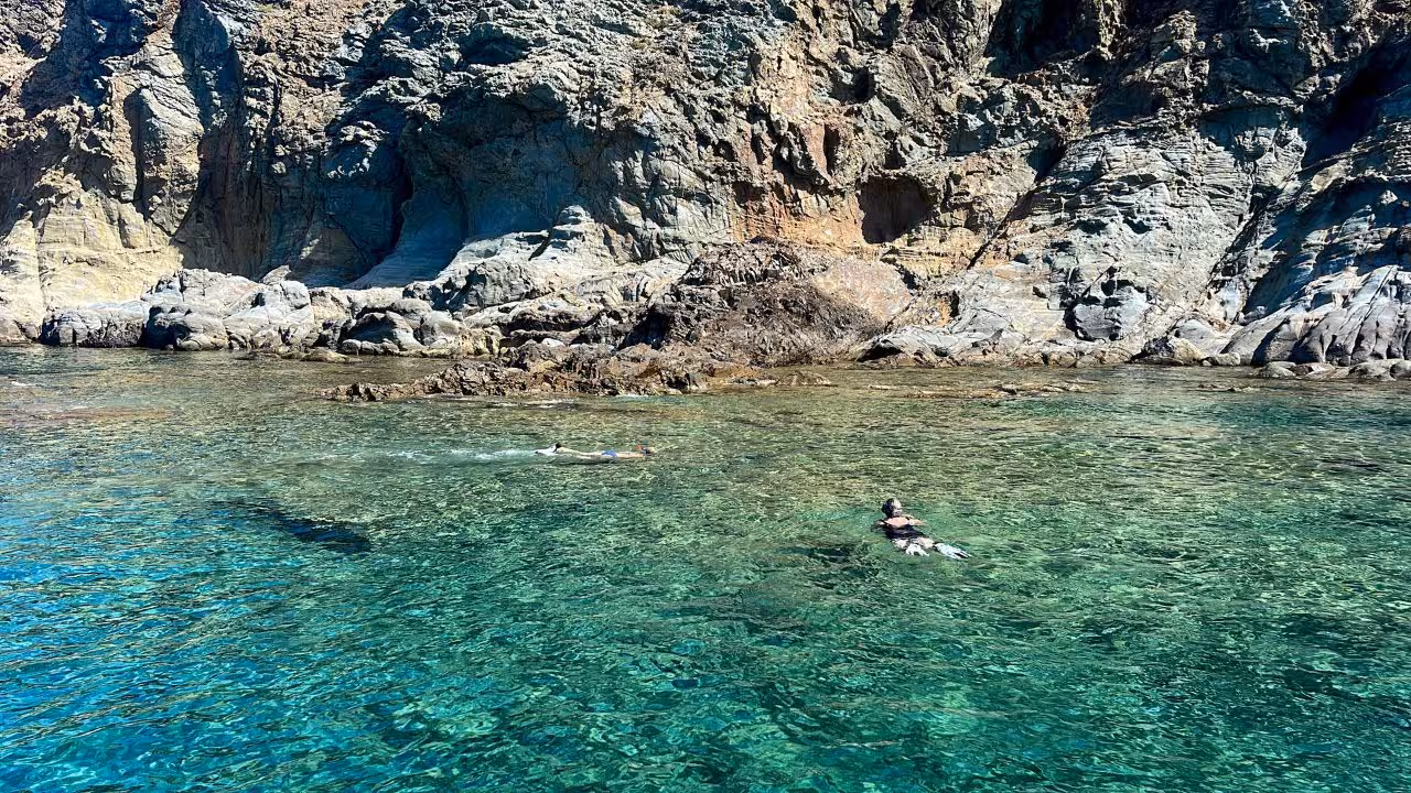 Snorkelers exploring the clear turquoise waters of Capo Marrargiu near rocky cliffs in Bosa, Sardinia.