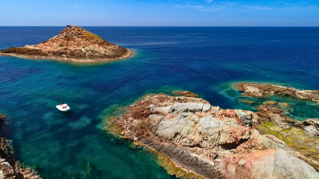 Aerial view of Capo Marrargiu's rugged coastline and a small boat in the serene blue waters near Bosa.