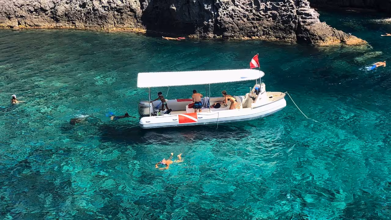 Tourists snorkelling near a boat in the clear turquoise waters of Capo Marrargiu, off the coast of Bosa.