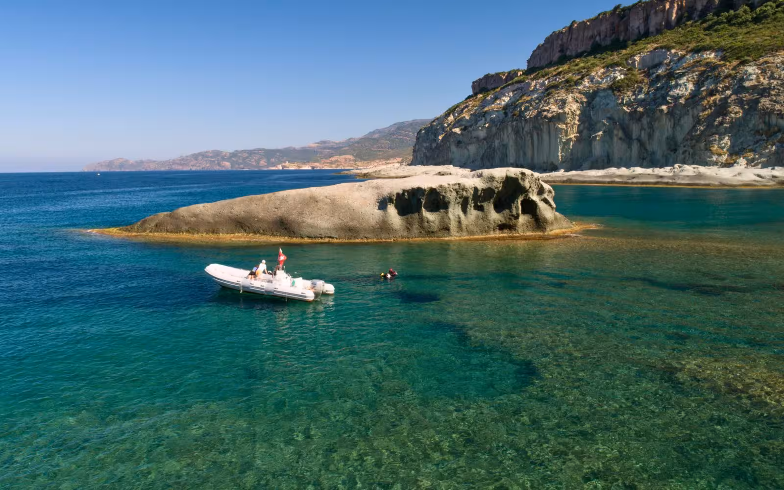 A boat near a rocky island in Bosa's clear waters, ideal for a diving baptism experience.