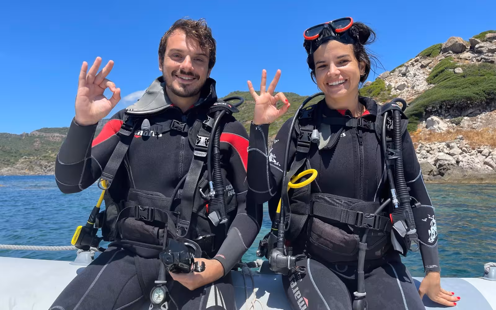 Smiling divers give the OK sign on a boat in Bosa, ready for an exciting diving baptism adventure.