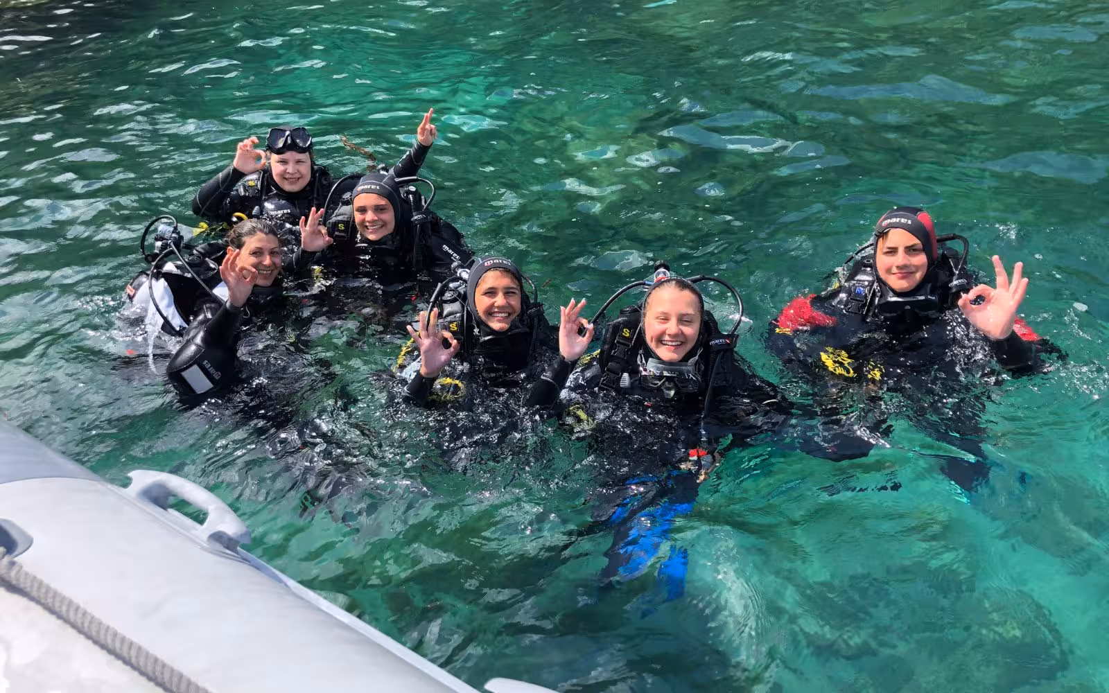 Group of divers in wetsuits giving okay signs, enjoying Bosa's diving baptism tour.
