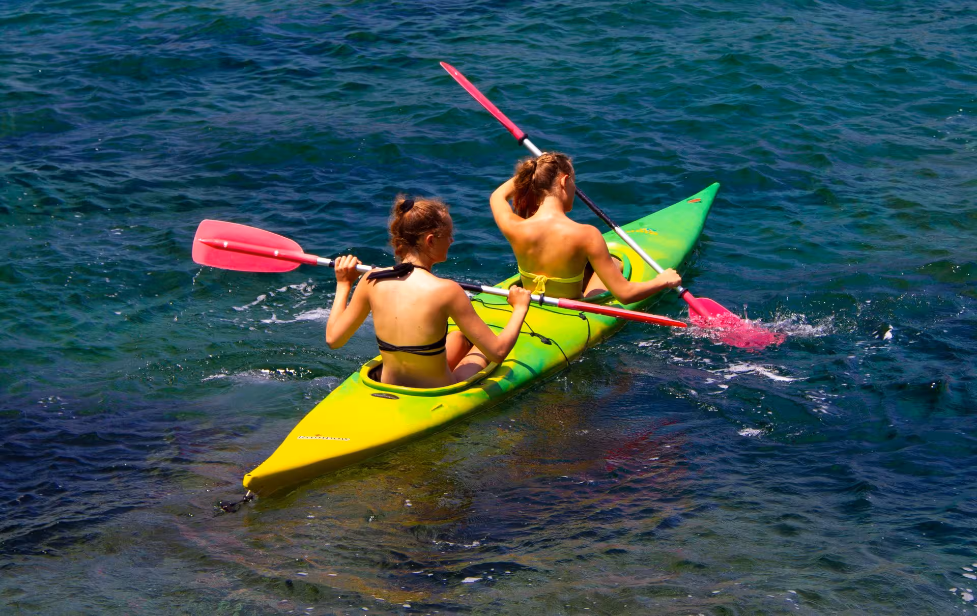 Two women kayaking in a vibrant green kayak on the Temo River, experiencing a memorable Bosa waterway tour.