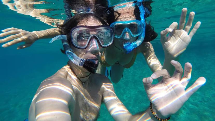 Two snorkelers giving an OK sign underwater in the crystal-clear waters of Capo Marrargiu, Bosa snorkelling tour.