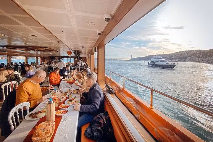 Private table dining on Bosphorus dinner cruise with Istanbul waterfront views through panoramic windows at sunset