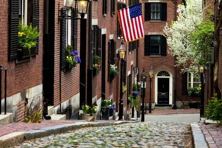 Cobblestone Acorn Street in Boston's Beacon Hill with red brick rowhouses, flower boxes, and American flag