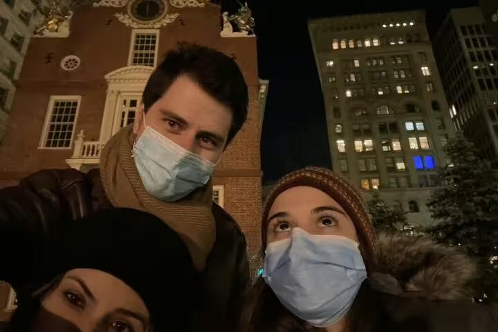 Three visitors wearing masks on Boston Freedom Trail at night with Old State House in background