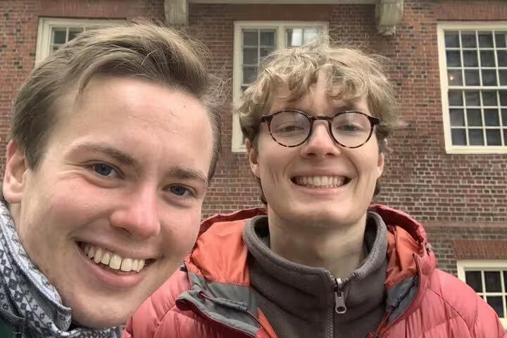 Two smiling visitors taking a selfie in front of a historic red brick building on the Boston Freedom Trail