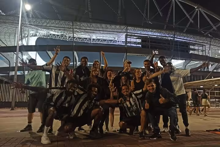 Group of Botafogo fans pose outside Nilton Santos Stadium at night on Rio de Janeiro locals soccer game tour