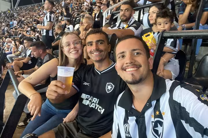 Travelers with locals in Botafogo jerseys cheer in Rio stadium stands during a live soccer match experience