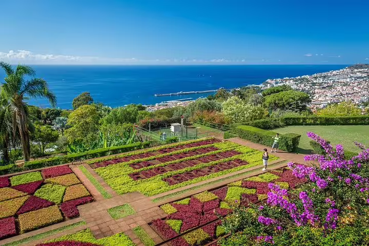 Vibrant botanical garden with ocean view, showcasing colorful geometric flower beds and lush greenery.