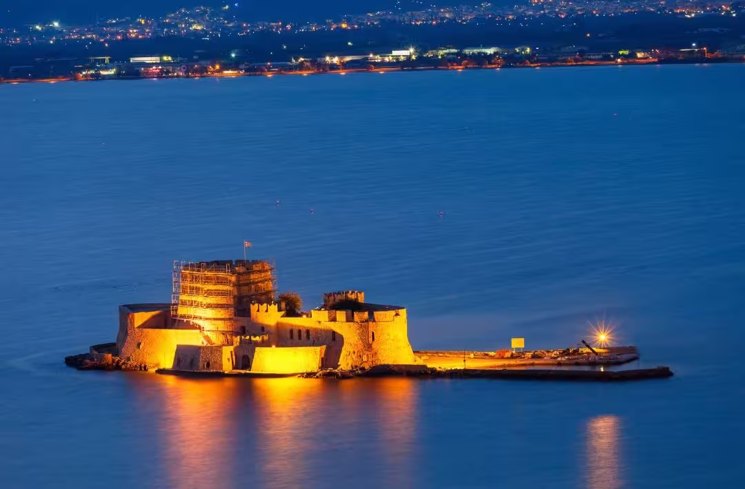 Illuminated Bourtzi Castle in Nafplio, Greece, at night, surrounded by calm sea, highlights Peloponnese day trip allure.