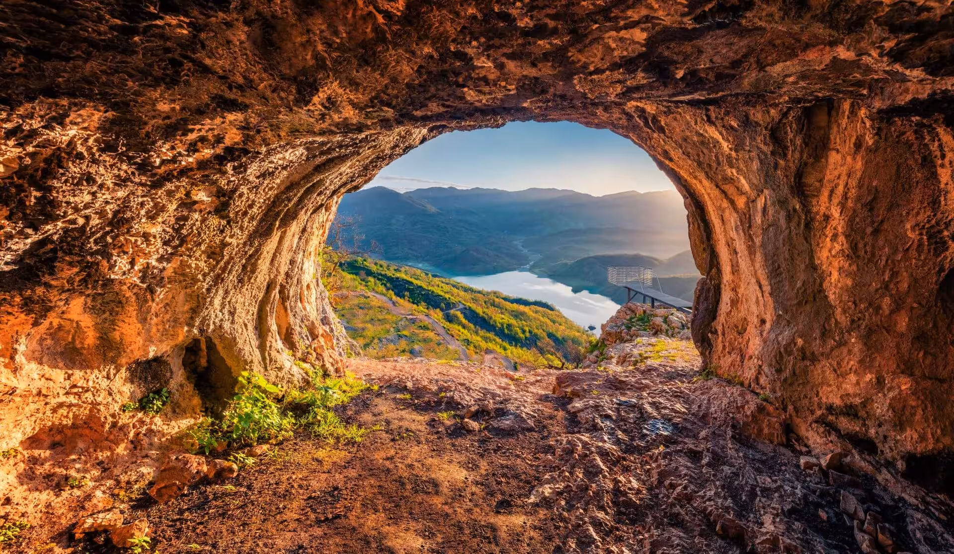Stunning cave entrance view overlooking Bovilla Lake and mountains, capturing nature's beauty on a day trip.